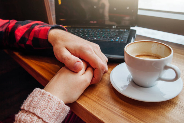 Νεαρό ζευγάρι κρατά τα χέρια και απολαμβάνει καφέ στο καφέ ενώ χρησιμοποιώντας ένα φορητό υπολογιστή - Φωτογραφία, εικόνα
