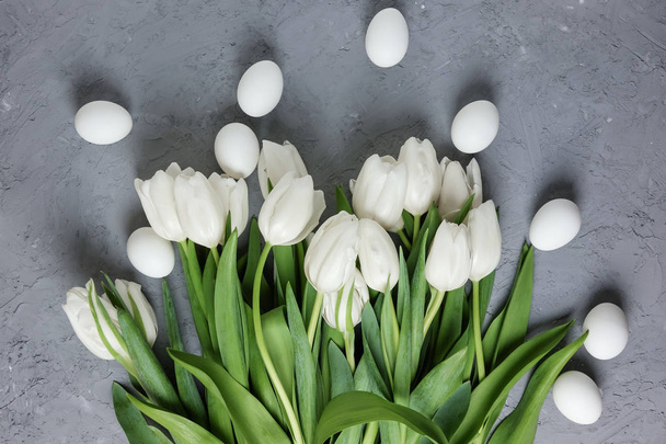 A bouquet of white tulips with chicken eggs on a gray concrete background. Top view. Flat lay. Postcard for Easter and Spring Holidays. - Foto, imagen
