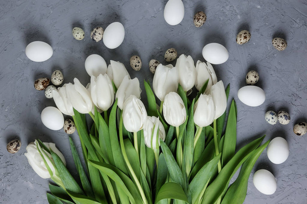 A bouquet of white tulips and chicken and quail eggs on a gray concrete background. Top view. Flat lay. Postcard for Easter and Spring Holidays. - 写真・画像