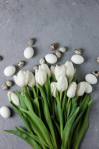A bouquet of white tulips and chicken and quail eggs on a gray concrete background. Top view. Flat lay. Postcard for Easter and Spring Holidays. - Photo, Image