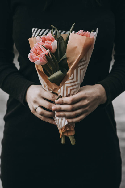 Woman hand holding soft pink tulips flowers bouquet decorated with kraft paper - Foto, Imagen