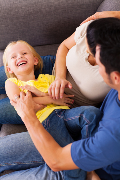 Parents tickling little daughter on sofa - Φωτογραφία, εικόνα