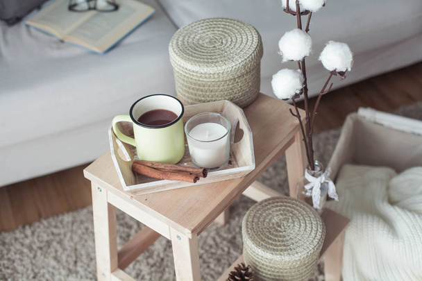 Home decor. A wooden bedside table, a sofa, a cotton, a mug of hot coffee, a knitted plaid. Warm house. Autumn. Cozy. House. The book and glasses. Interior. - Photo, Image