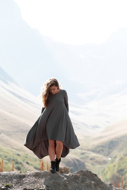 A beautiful girl in a flying dress is standing by a cliff in the mountains - Foto, Imagem