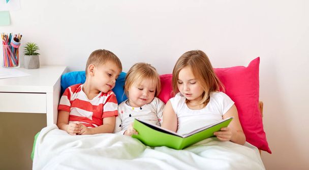 niños pequeños leyendo libro en la cama en casa
 - Foto, Imagen