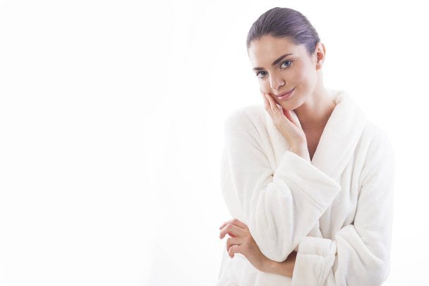 Beautiful and natural woman in white bathrobe is touching her skin. Relax and comfortable feelings only. - Photo, Image