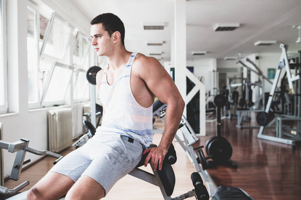 Young attractive adult man exercising and doing weight lifting at fitness gym. Sport training indoors - Φωτογραφία, εικόνα