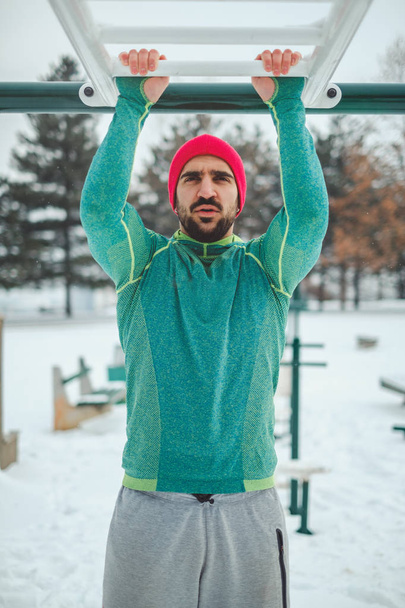 Man doet bovenhandse kin ups buiten op een besneeuwde dag - Foto, afbeelding