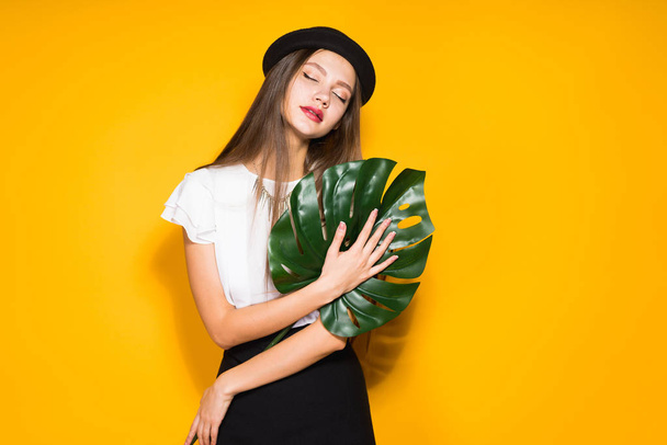 woman on a yellow background holds a large leaf - Фото, изображение