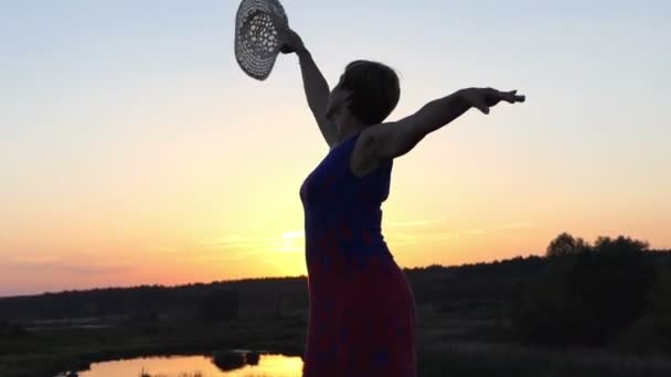 Μέσης ηλικίας γυναίκα χορούς σε μια τράπεζα στη λίμνη στο ηλιοβασίλεμα - Πλάνα, βίντεο