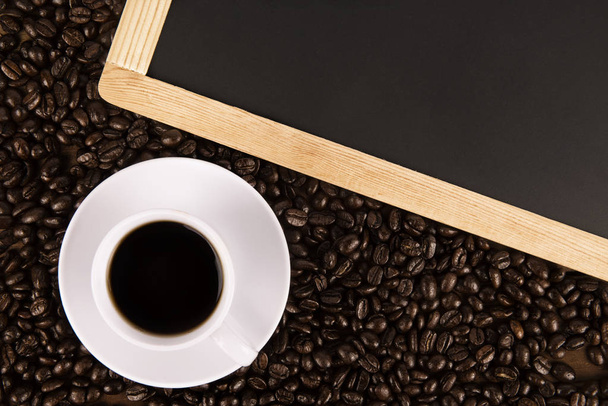 Cup of coffee and coffee beans on old wooden background, black board on top. Directly above. - 写真・画像