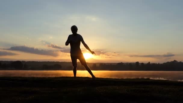glücklicher Mann tanzt Freestyle auf einem Seeufer bei Sonnenuntergang im Slo-mo - Filmmaterial, Video