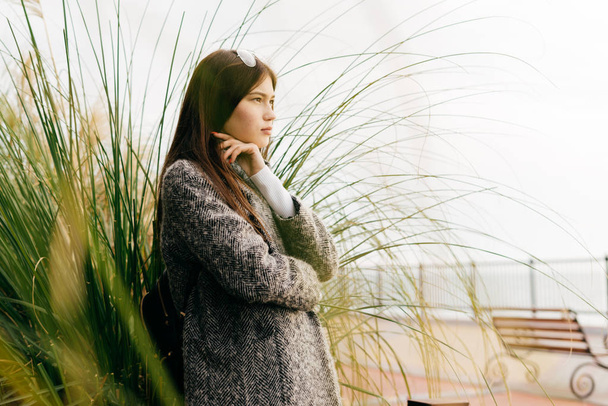 pensive woman stands against a background of plants, street fashion - Fotó, kép