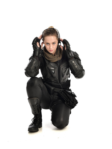 Ganzes Porträt einer Soldatin in schwarzer taktischer Rüstung, sitzend, isoliert auf weißem Studiohintergrund. - Foto, Bild
