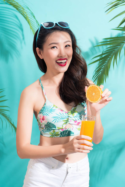 Young asian woman drinking juice from glass standing on blue background - Photo, Image