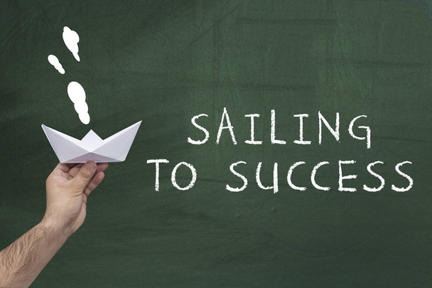 Лідерство, бізнес, концепція успіху. Рука людини тримає паперовий човен проти зеленої дошки з текстом: вітрильний спорт до успіху
. - Фото, зображення