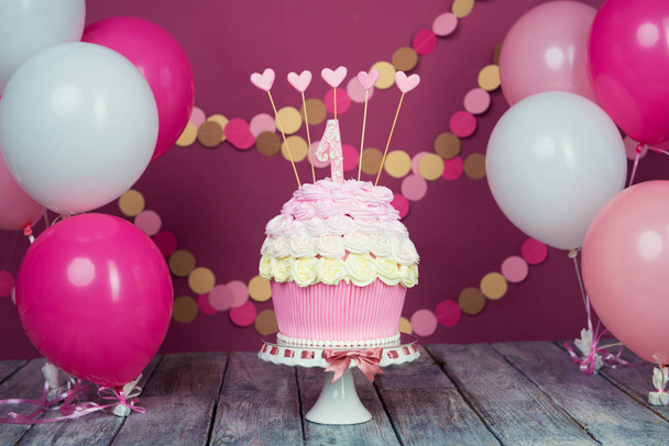 Egy egység egy rózsaszín háttér, labdák és papír koszorú első születésnapi torta. - Fotó, kép