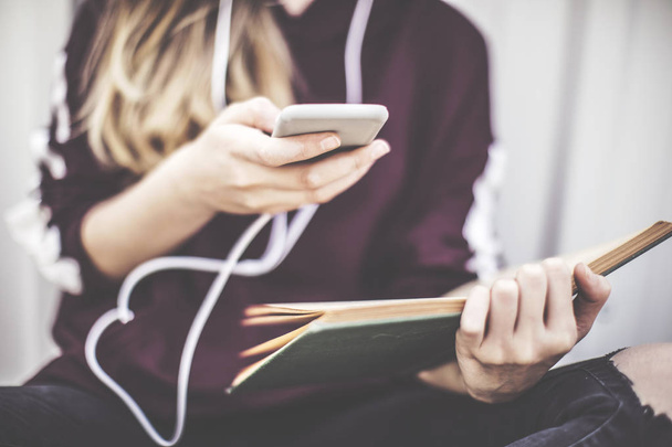 junges Mädchen benutzt Handy und liest draußen Buch - Foto, Bild