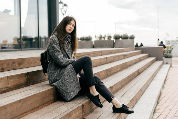 beautiful young woman sitting on the steps, street fashion - 写真・画像