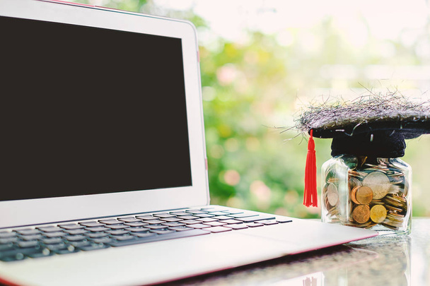 Computer laptop and square academic cap with the glass jar of co - Photo, Image