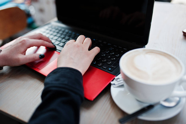 Закройте руки девушки, работающей с красным ноутбуком с чашкой каппу
 - Фото, изображение