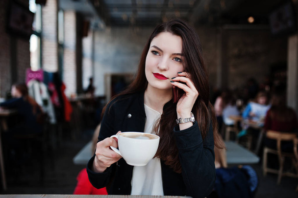 Brunette girl sitting on cafe with cup of cappuccino and speakin - Foto, afbeelding