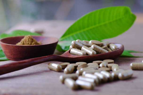 трав'яний препарат в таблетках і капсулі на дерев'яному столі з зеленим листям
  - Фото, зображення