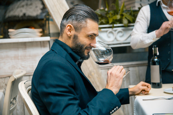 handsome bearded rich man with stylish mustache and beard holding glass and sniff smell of red wine at the restautant. - Photo, Image