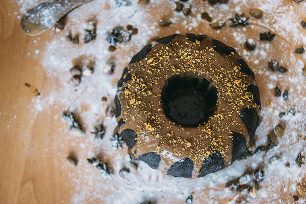 black  cake on the wooden table with nuts and powdered sugar and flour - Photo, Image