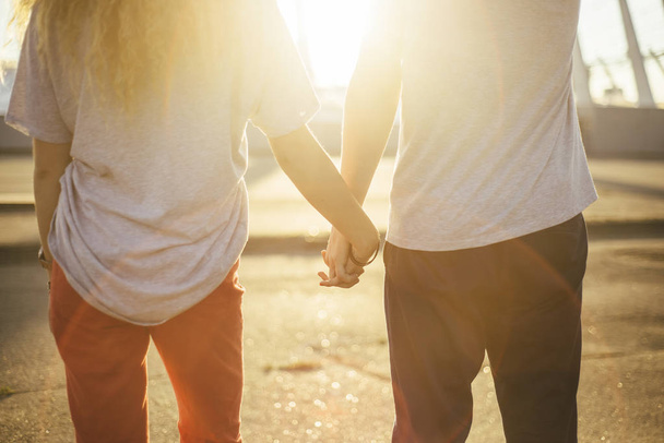 赤と濃いジーンズで素敵なカップルが、手を握るし、太陽を見て - 写真・画像