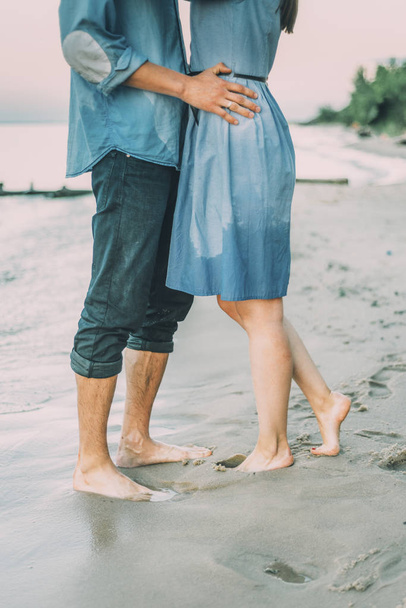 casal está abraçando e ficar perto à beira-mar com céu cinza e árvores verdes
 - Foto, Imagem