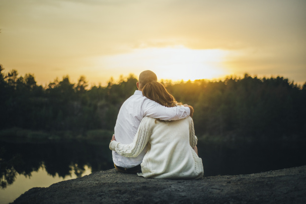 couple is hugging in white shirt and sweater looking to the yellow sunset sitting - Fotó, kép