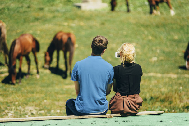 couple is making selfie on smarphone sitting near the horses - Photo, Image