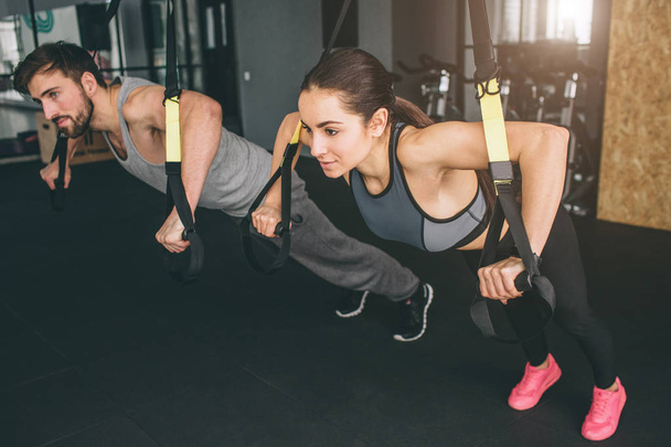 Young woman and man are doing TRX chest press exercises. They are sport partners and doing all exercises together. Close up. Cut view. - 写真・画像