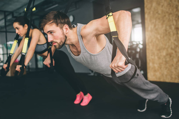Young man and woman are doing TRX chest press exercise. He is doing push up while she is doing oush down. Close up. Cut view. - Fotografie, Obrázek