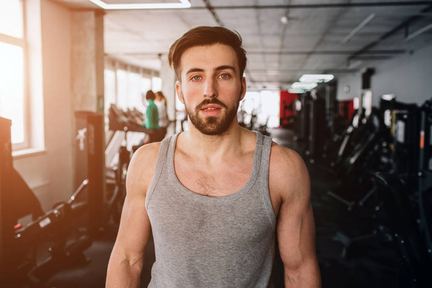 Close up of a stong and good-looking man standing in gym and looking straight forward. He has some rest after hard workout. Cut view. - Fotó, kép