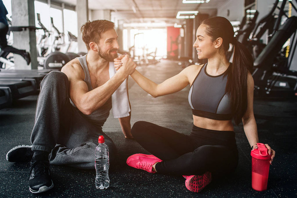 Sweet and tender picture of two beloved people sitting on the floor in the gym close to each other. They look lovely and happy to be together - Фото, изображение