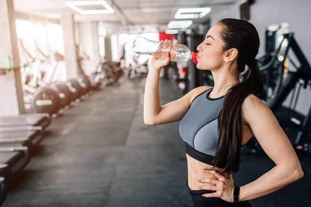 Close up of a beautiful girl drinking water from the bottle. He is having some rest after workout. Cut view. - Foto, Imagen