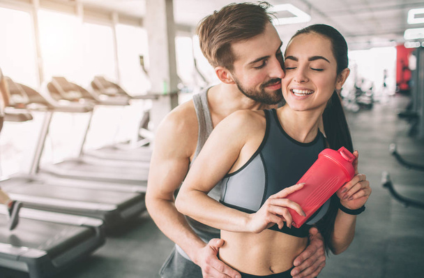Amazing couple standing in the gym. The guy is hugging his girlfriend. She looks happy. Close up. Cut view. - Фото, изображение