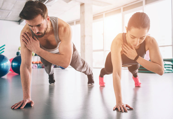 Slim girl and strong man are standing in one hand plank position and balancing on that hand. They look concentrated and concious. - Foto, Imagem