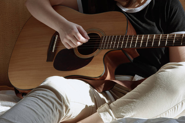 Jovem tocando guitarra e sentada na cama
 - Foto, Imagem