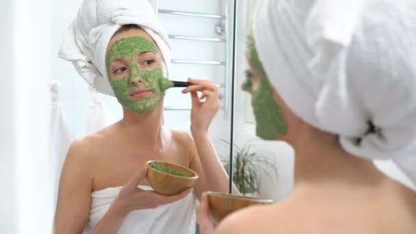 a young woman with a white towel put on her face a green moisturizing mask - Felvétel, videó