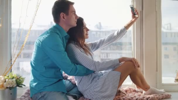 Gelukkig vrolijke verliefde paar maken selfie op venster, jonge aantrekkelijke jongen en meisje - Video