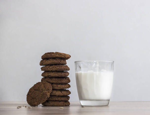 on a wooden table on a white background stands a stack of oatmeal cookies sunflower seeds a glass of milk - Photo, image