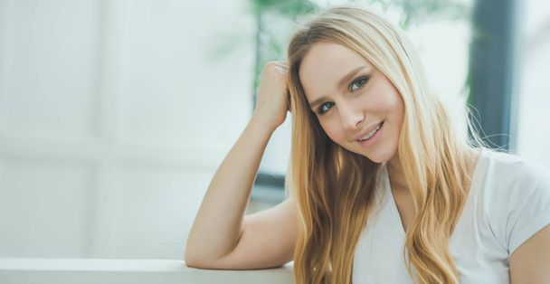 Close up Portrait of a beautiful smiling young blond woman sitting at home on a sofa and resting or relaxing. - Fotografie, Obrázek