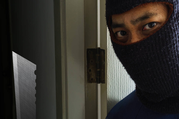 ドアの後ろに隠れているナイフで覆面をした強盗 - 写真・画像