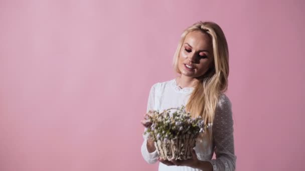 Blonde young woman in elegant white dress. Girl posing on background with handbag. Lady with spring bouquet of flowers. Fashion. Ukrainian girl with flowers. - Filmati, video