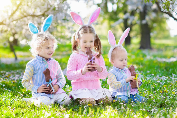 Kert húsvéti tojás vadászat. Gyerekek enni csoki nyuszi. - Fotó, kép