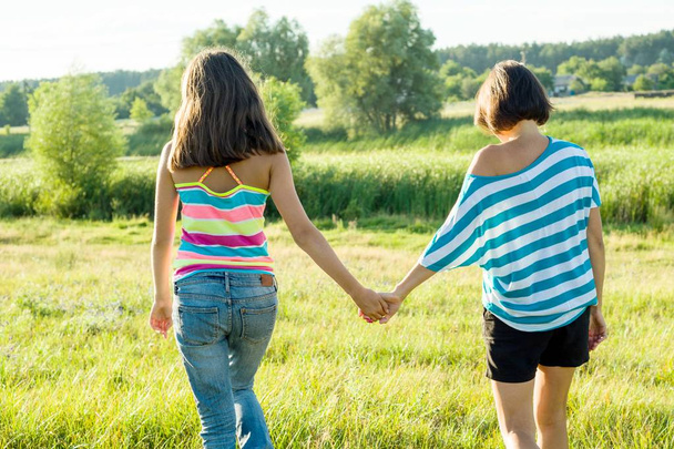 Mother and teen daughter holding hands, back view. Photo on nature in a sunny summer day. - Φωτογραφία, εικόνα