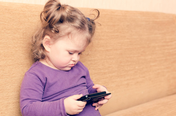Little girl playing smartphone sitting on sofa - Foto, Bild